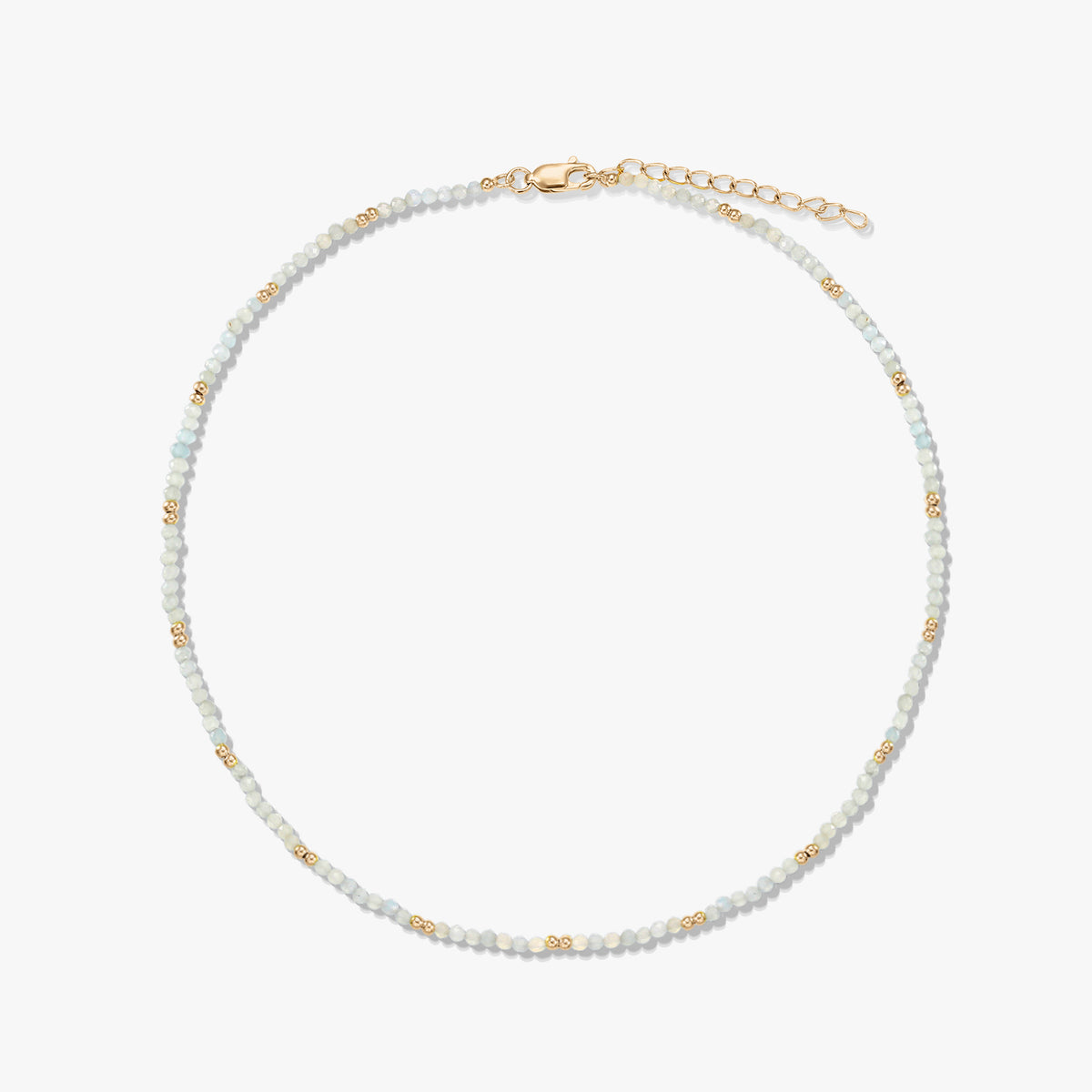 Delicate beaded moonstone necklace with small gold spacer beads and a gold‑plated sterling silver lobster clasp and extender, arranged in a circle on a white background.