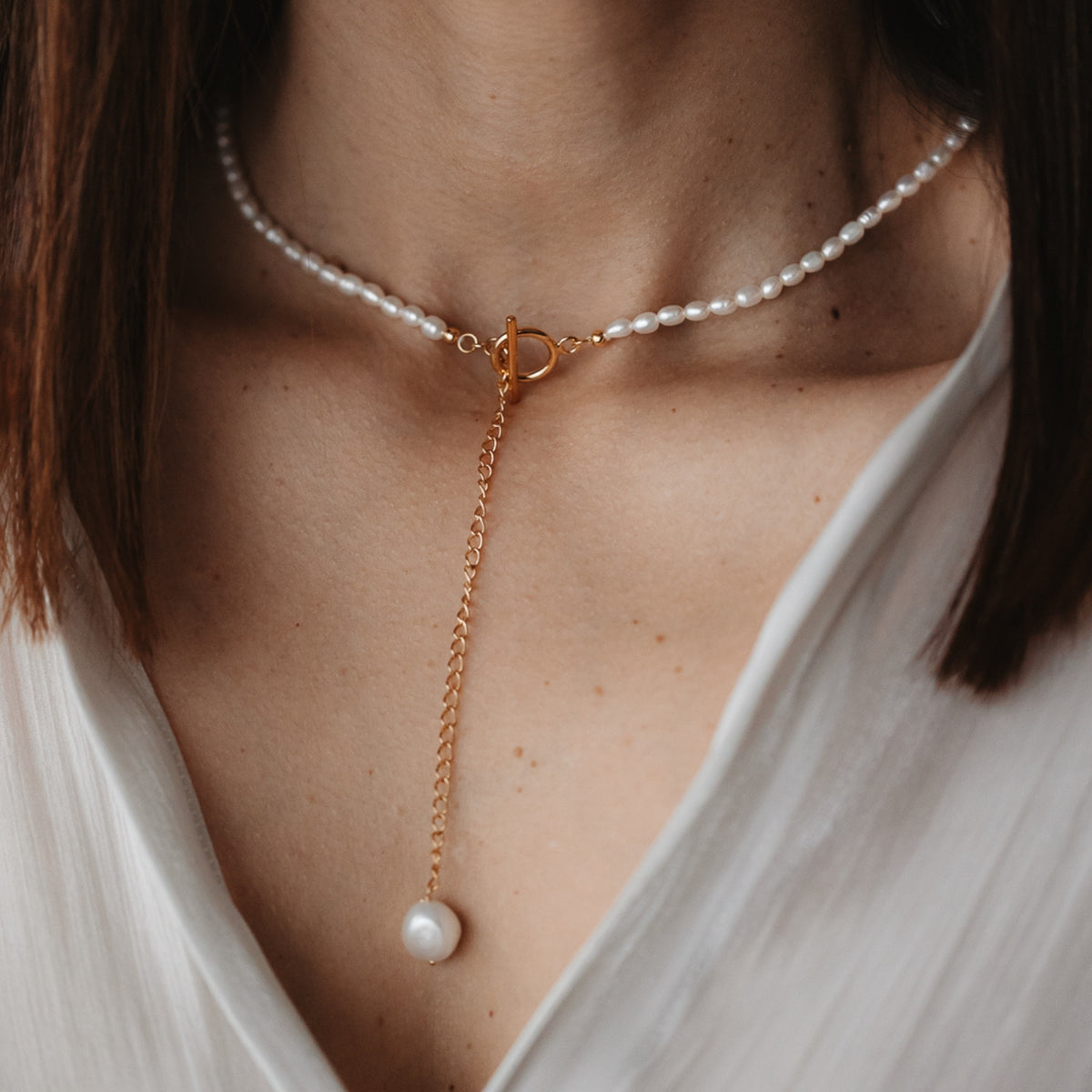 Close-up of a woman's neck wearing a silver necklace with a natural pearl pendant and gold chain.