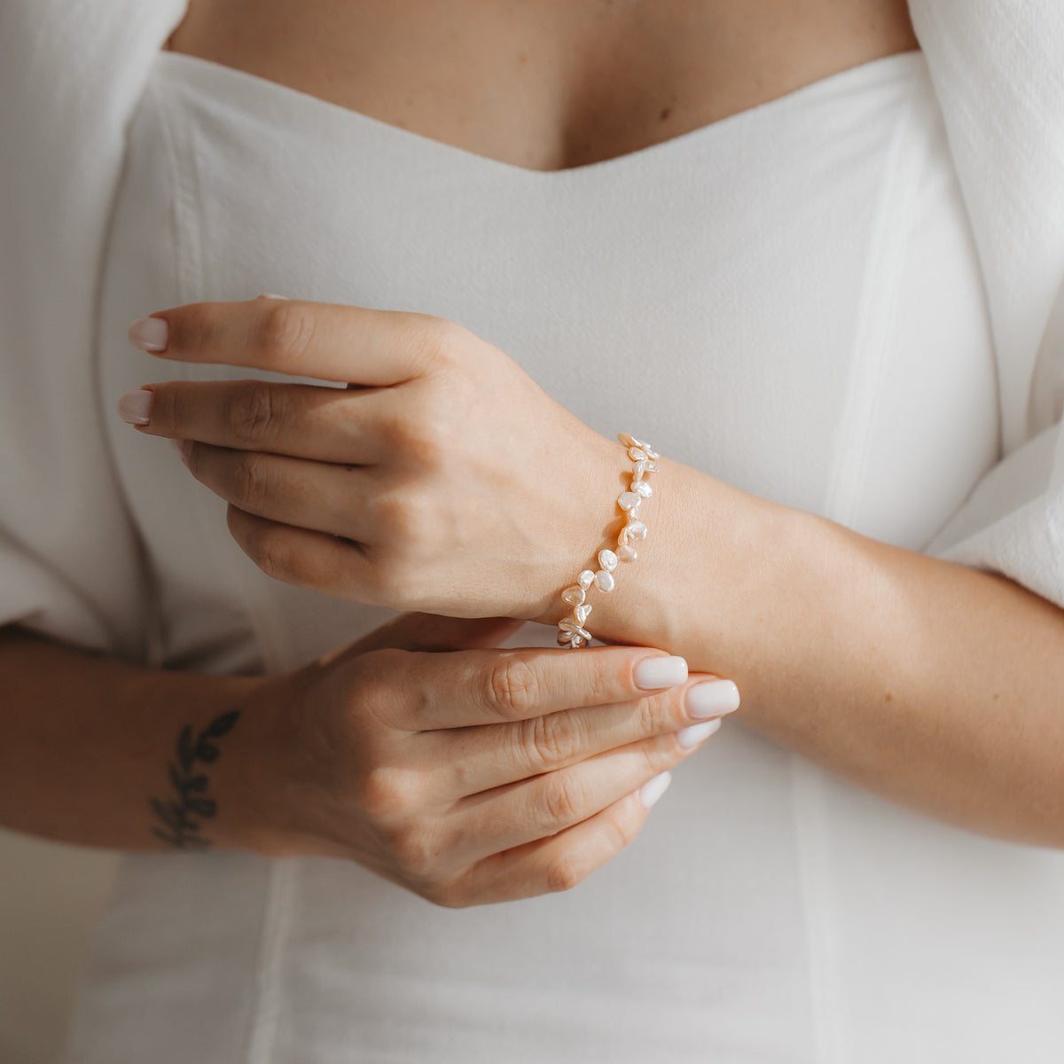 Close-up of hands wearing a delicate sterling silver bracelet with pink keshi pearls, styled with a white dress.