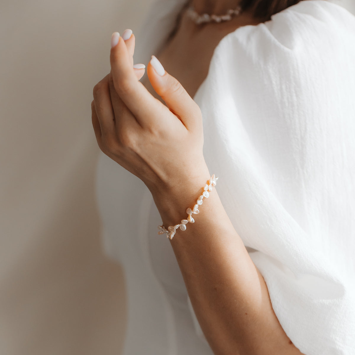 Close-up of a person's wrist wearing a gold‑plated sterling silver bracelet with pink keshi pearls, styled with a white puff‑sleeve top.