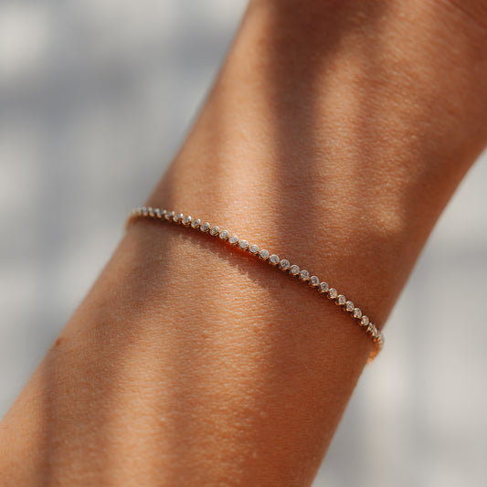 Close-up of a delicate 14K yellow gold tennis bracelet with small round diamonds worn on a wrist, lit by soft natural light.