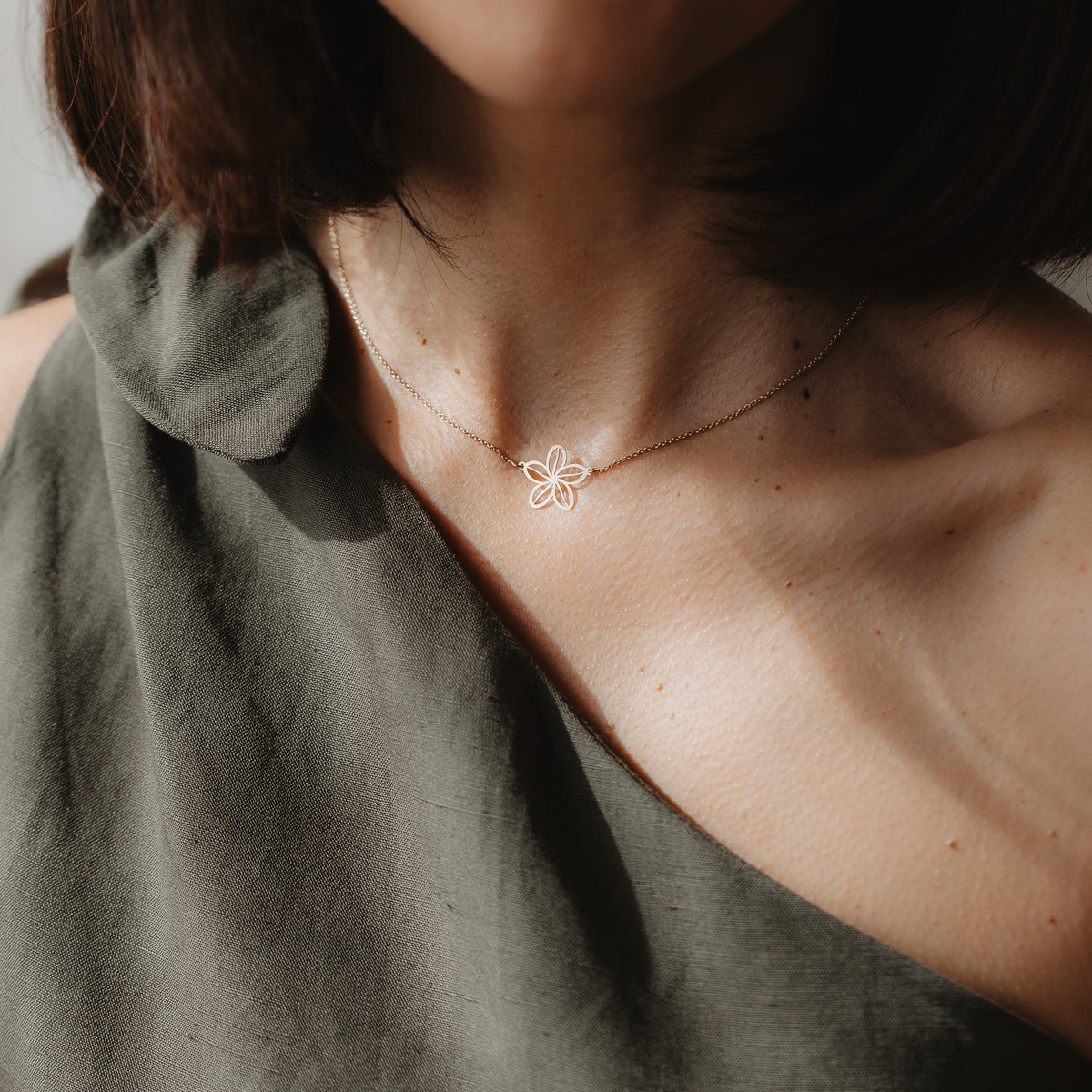 Close-up of a model wearing the Wildflower 14K yellow gold necklace with a delicate flower outline pendant, shown at the collarbone in natural light.