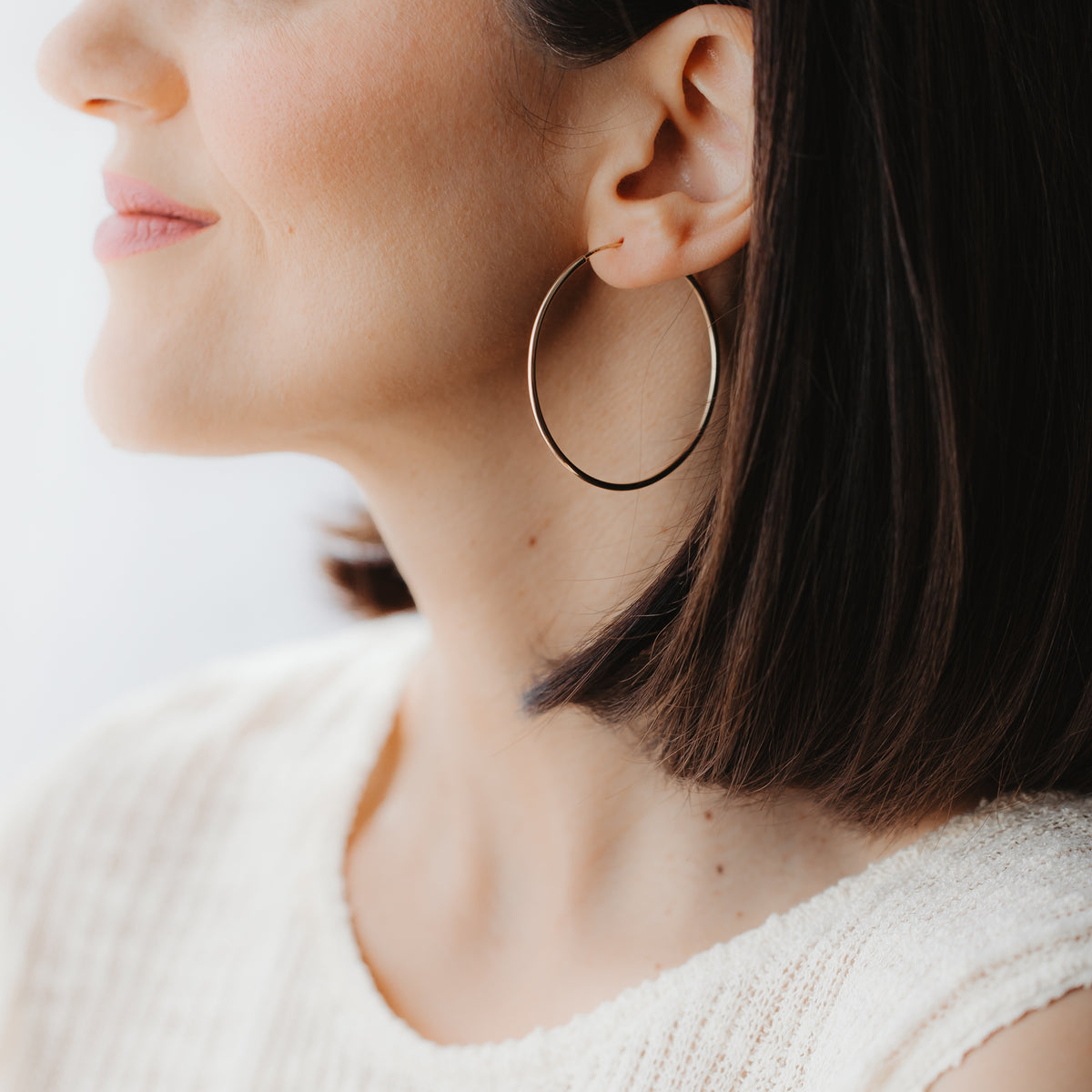 Close-up side profile of a model wearing a large 14k yellow gold hoop earring, shown on ear in soft natural light.