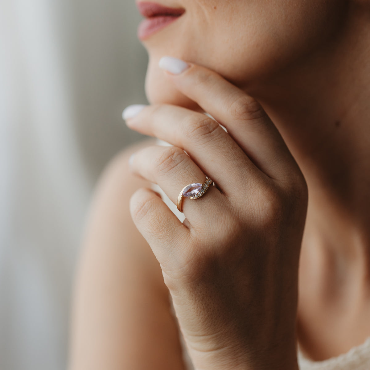 Close-up of a hand near the face wearing the Velvet Rose 14K yellow gold ring with a marquise pink sapphire and small accent diamonds.