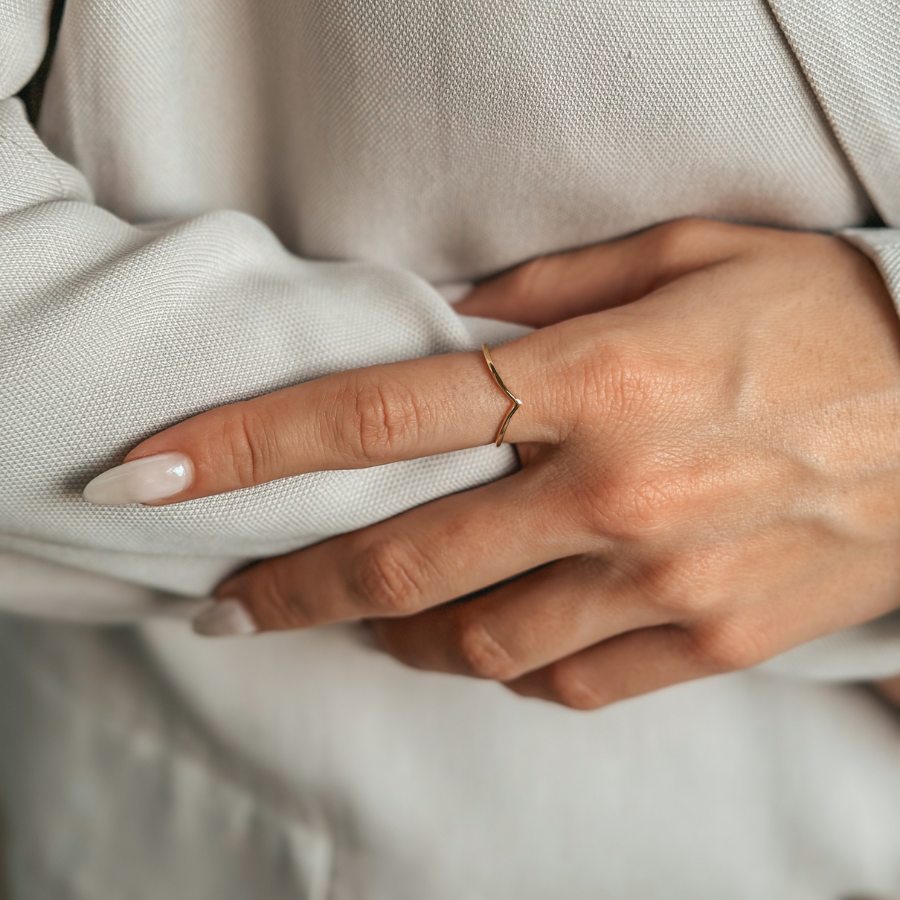 Close-up of a hand wearing a minimalist gold-plated silver ring over a light fabric background.