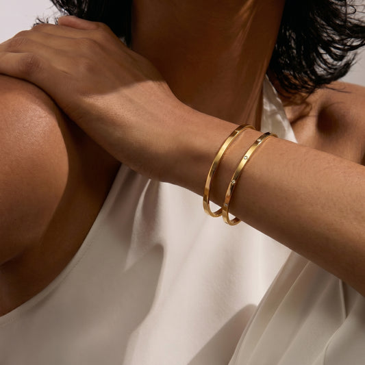 Close-up of a person's arm wearing two gold bangle bracelets on a white background.