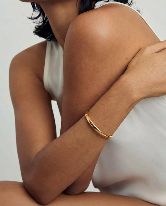 Close-up of a person wearing a golden silver bracelet on the arm, dressed in a white sleeveless top.