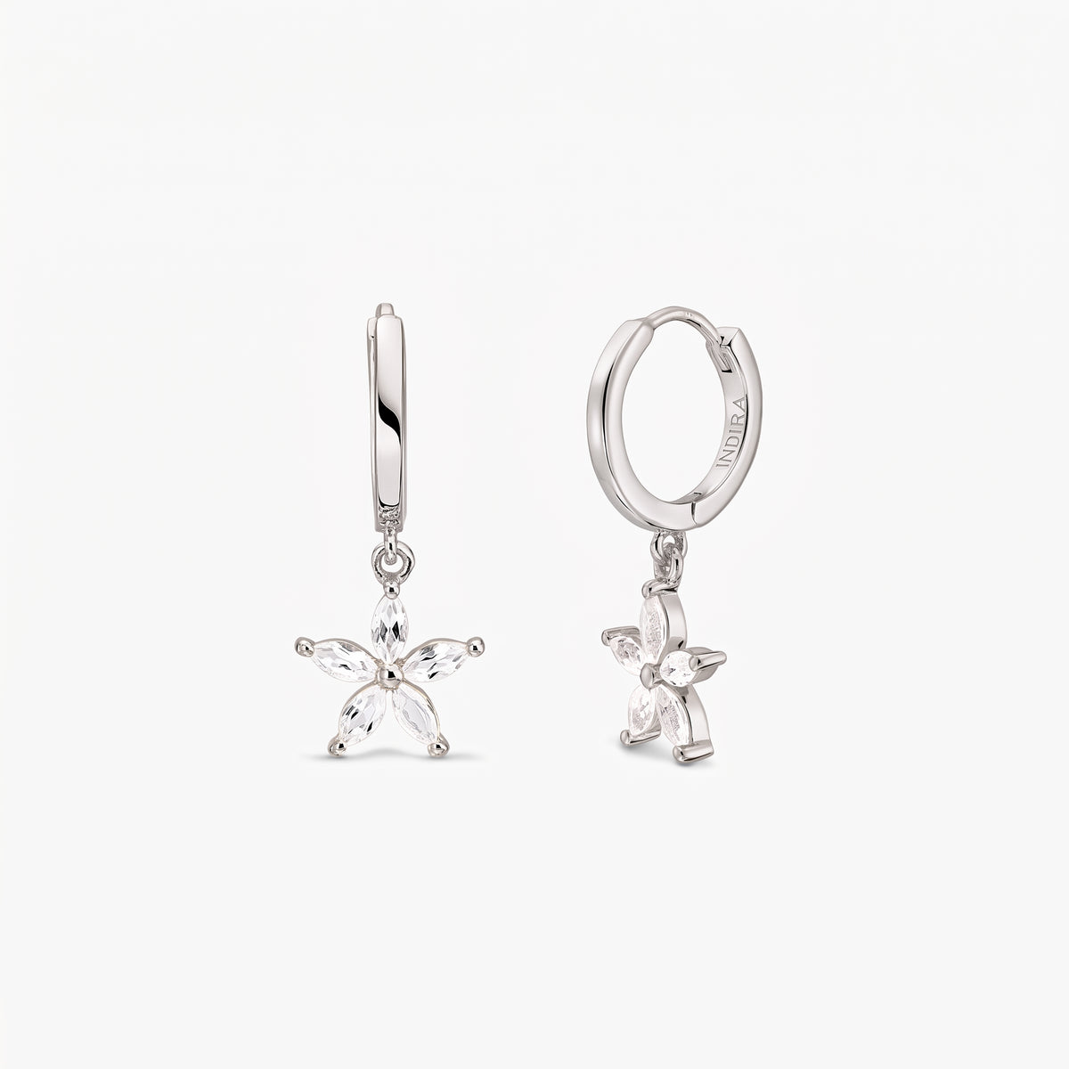 Pair of sterling silver huggie hoop earrings with dangling five‑petal blossom charms set with white topaz on a white background.