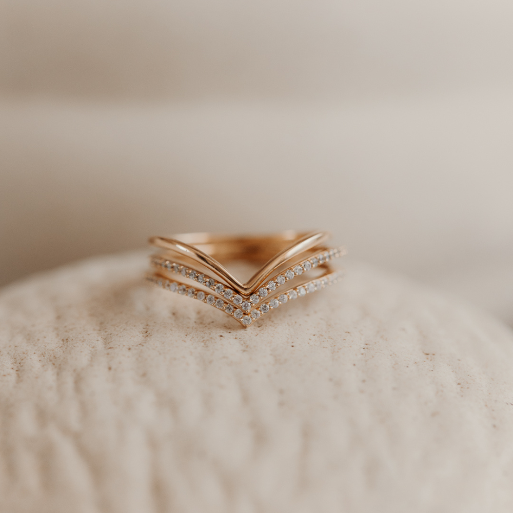 Minimalist gold-plated silver ring with a layered design on a textured surface.