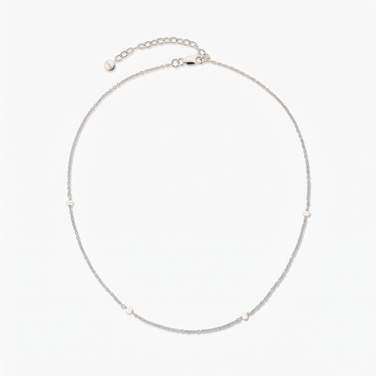 Delicate silver chain necklace with tiny white pearl stations, shown in a circle on a white background with an adjustable extender and lobster clasp.