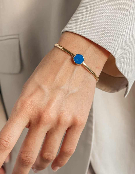 A close-up of a wrist wearing a gold bracelet featuring a blue hexagonal stone.