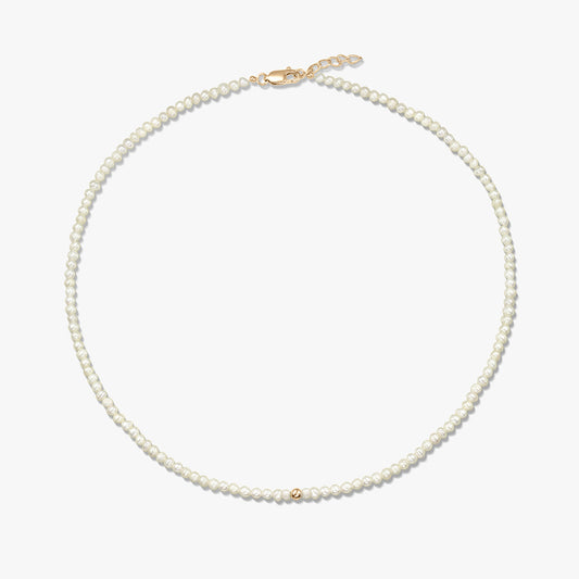 Square product image of a delicate natural pearl beaded necklace with a small 14K yellow gold bead accent and a yellow-gold lobster clasp with short extender, on a white background.