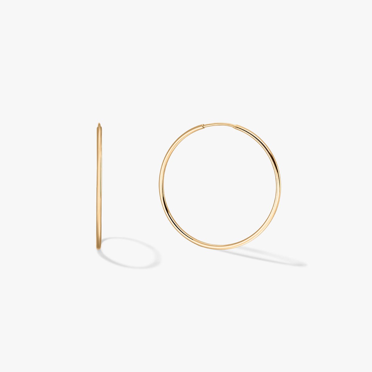 Pair of medium 14K yellow gold hoop earrings on a white background, one shown front-facing and one in side profile.