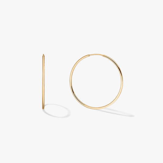 Pair of medium 14K yellow gold hoop earrings on a white background, one shown front-facing and one in side profile.