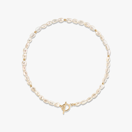 Studio photo of a natural pearl beaded necklace with small gold spacer beads and a gold-tone toggle clasp, arranged in a circle on a white background.