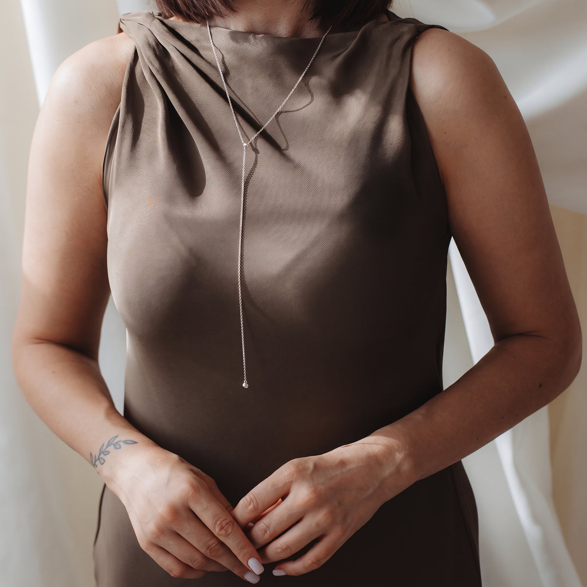 Close-up of a person wearing a sterling silver bola (lariat) necklace over a taupe satin dress in soft indoor light.
