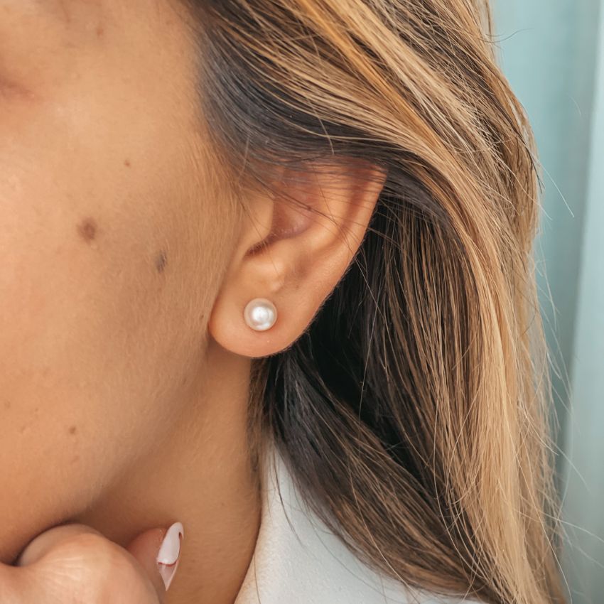 Close-up of an ear wearing a silver earring with a classic pearl.