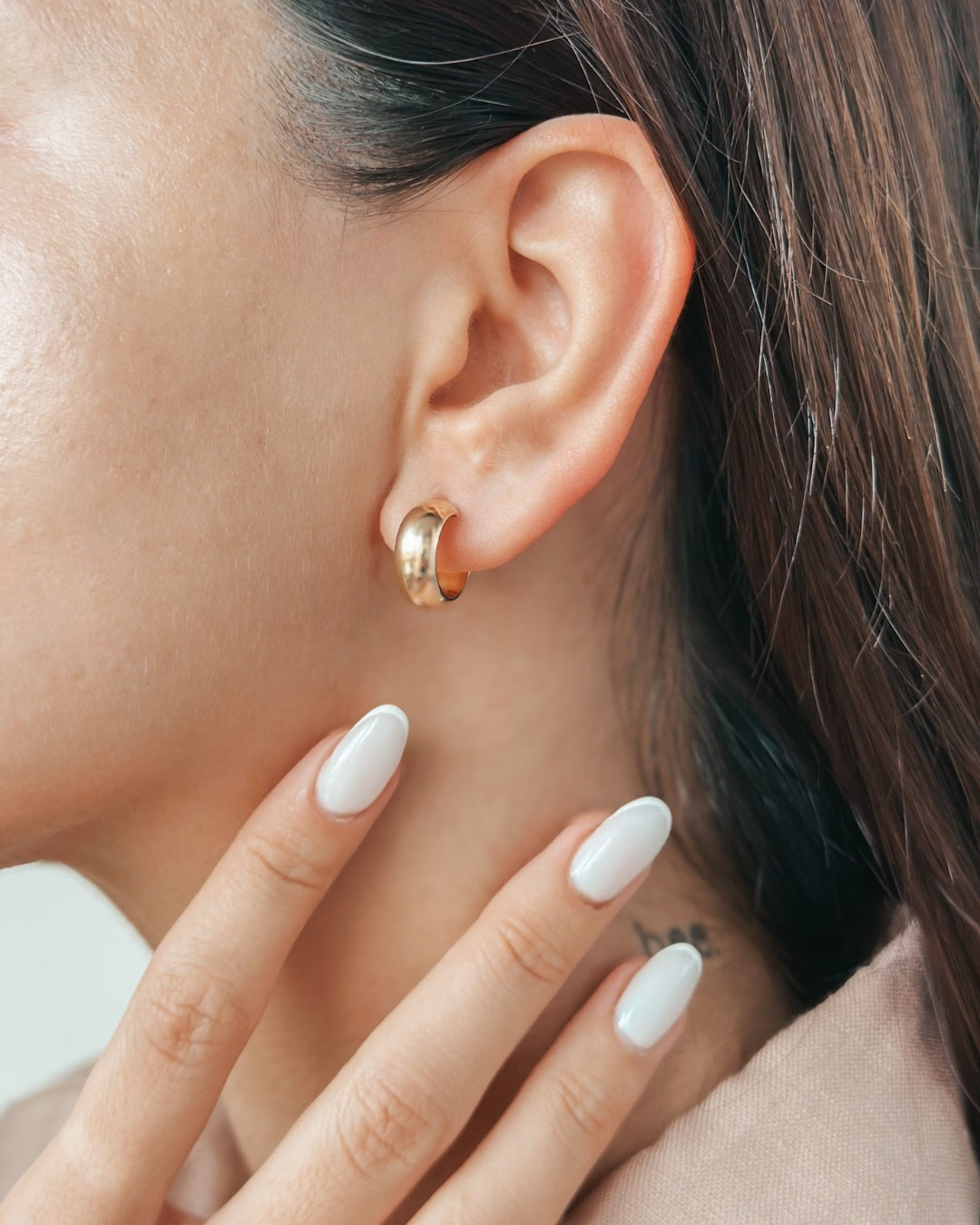 Close-up of a woman's ear wearing a gold hoop earring with manicured fingers touching her neck.