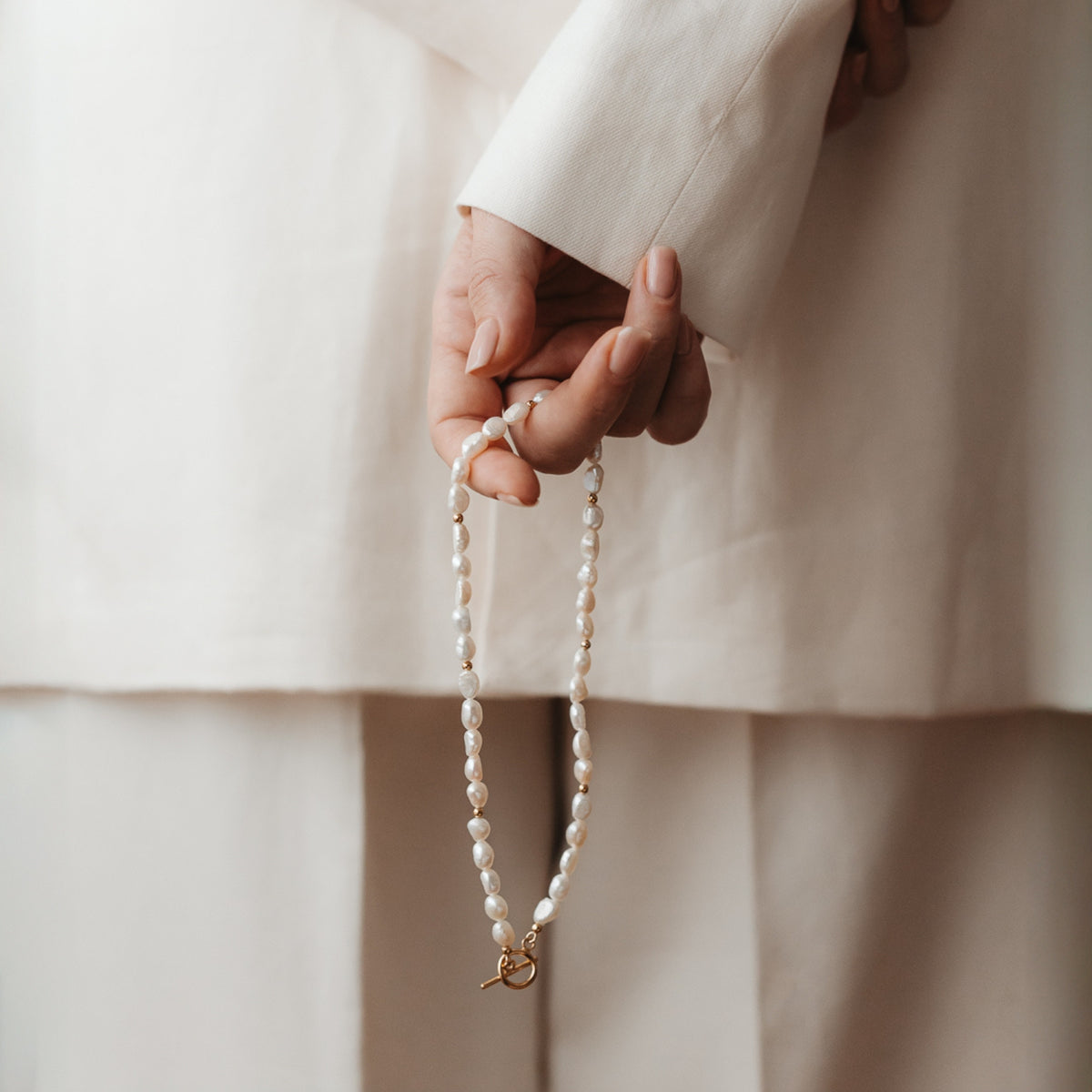 Close-up of a hand holding a silver necklace with natural pearls.
