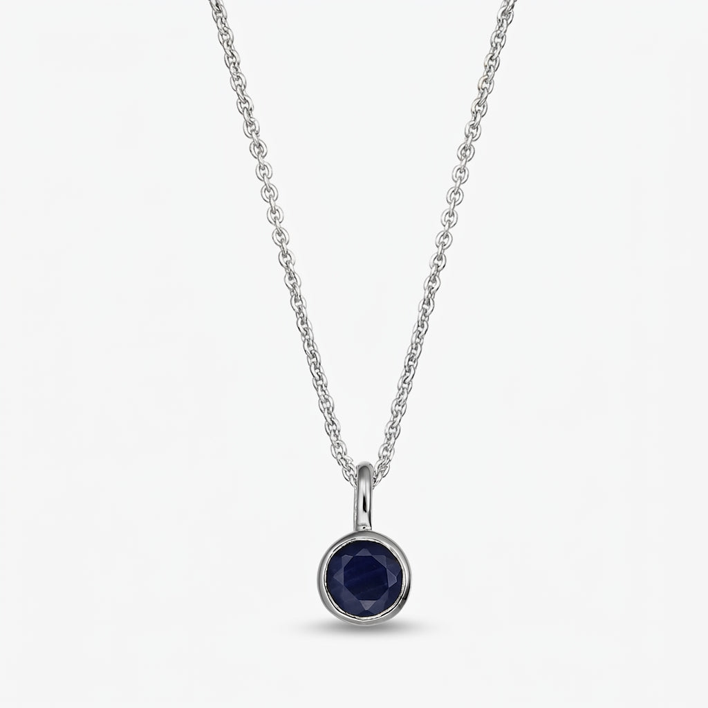 Sterling silver birthstone necklace with a small round bezel‑set dark blue sapphire pendant on a fine chain, isolated on white.