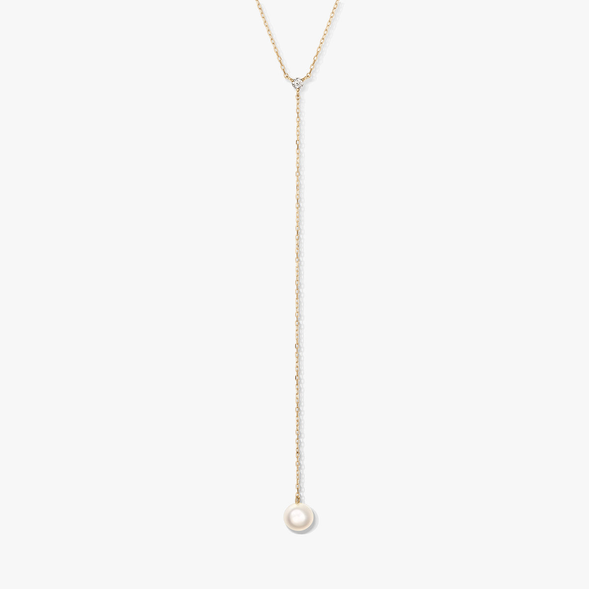 Minimalist gold lariat necklace with a single round white pearl drop and small accent stone, centered on a white background.