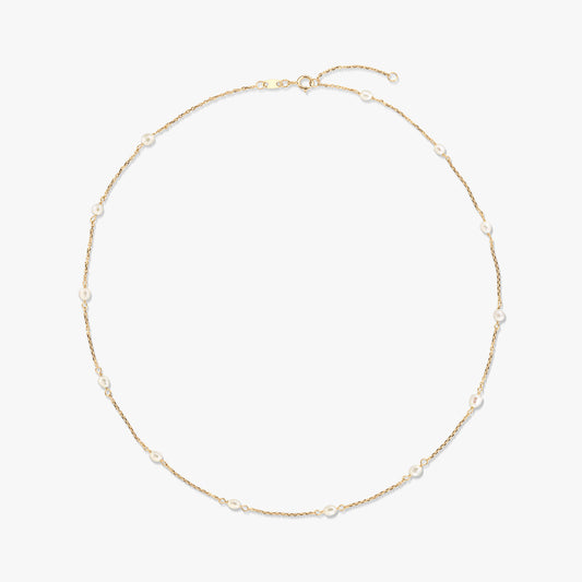 14K yellow gold station necklace with small natural white pearls spaced along a fine chain, isolated on a white background.
