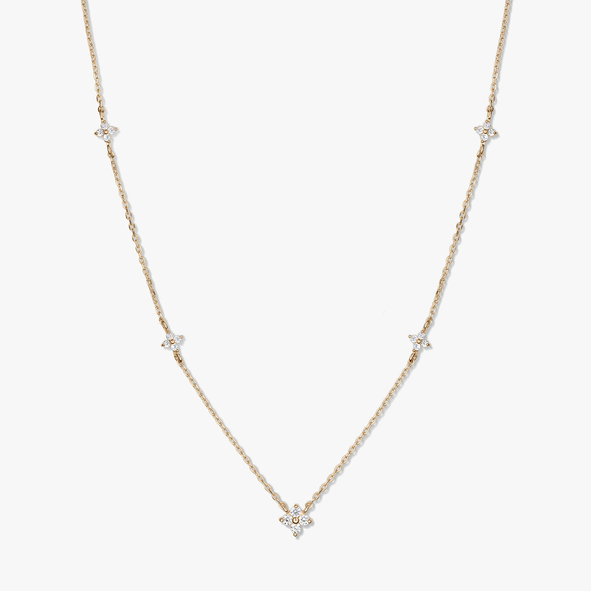 Delicate 14K yellow gold station necklace with small white zirconia clover motifs on a fine chain, photographed on a white background.