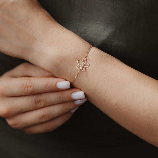 Close-up of a delicate 14K gold bracelet with an openwork wildflower charm on a wrist, against a dark fabric background.