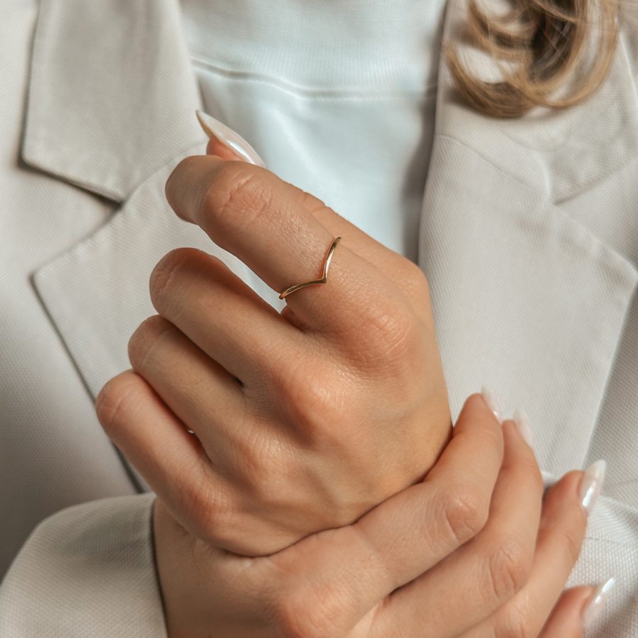 Close-up of a hand wearing a simple V-shaped gold-plated silver ring, with neutral-toned attire in the background.