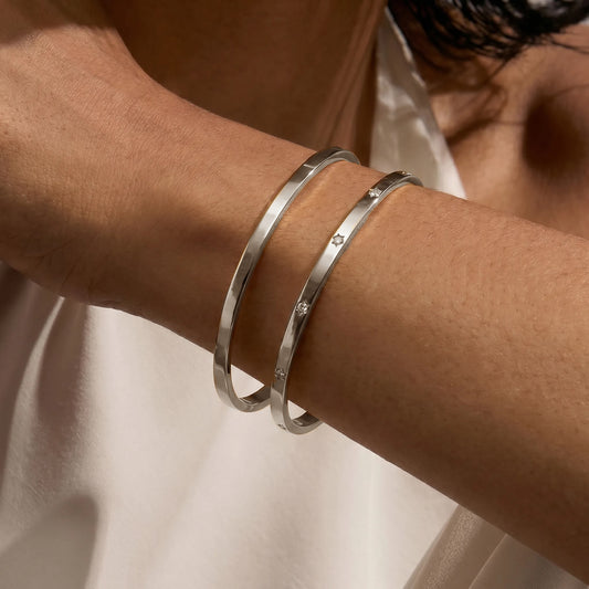 Close-up of a wrist adorned with two minimalist silver bracelets. One is plain, and the other features small zirconia stones.