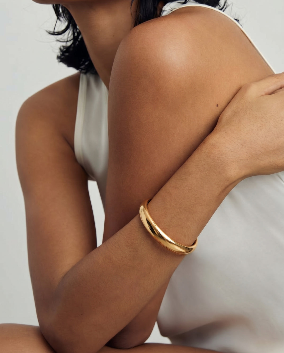 Close-up of a person wearing a gold-plated bangle bracelet on their arm, against a white background.