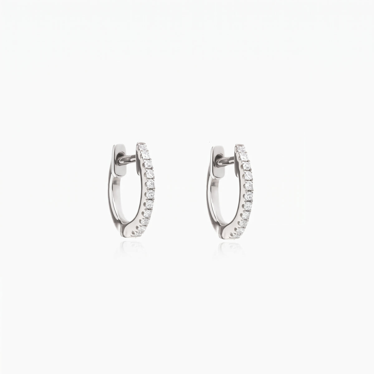 Pair of Sadie silver huggie hoop earrings with pavé clear zirconia on a white background.
