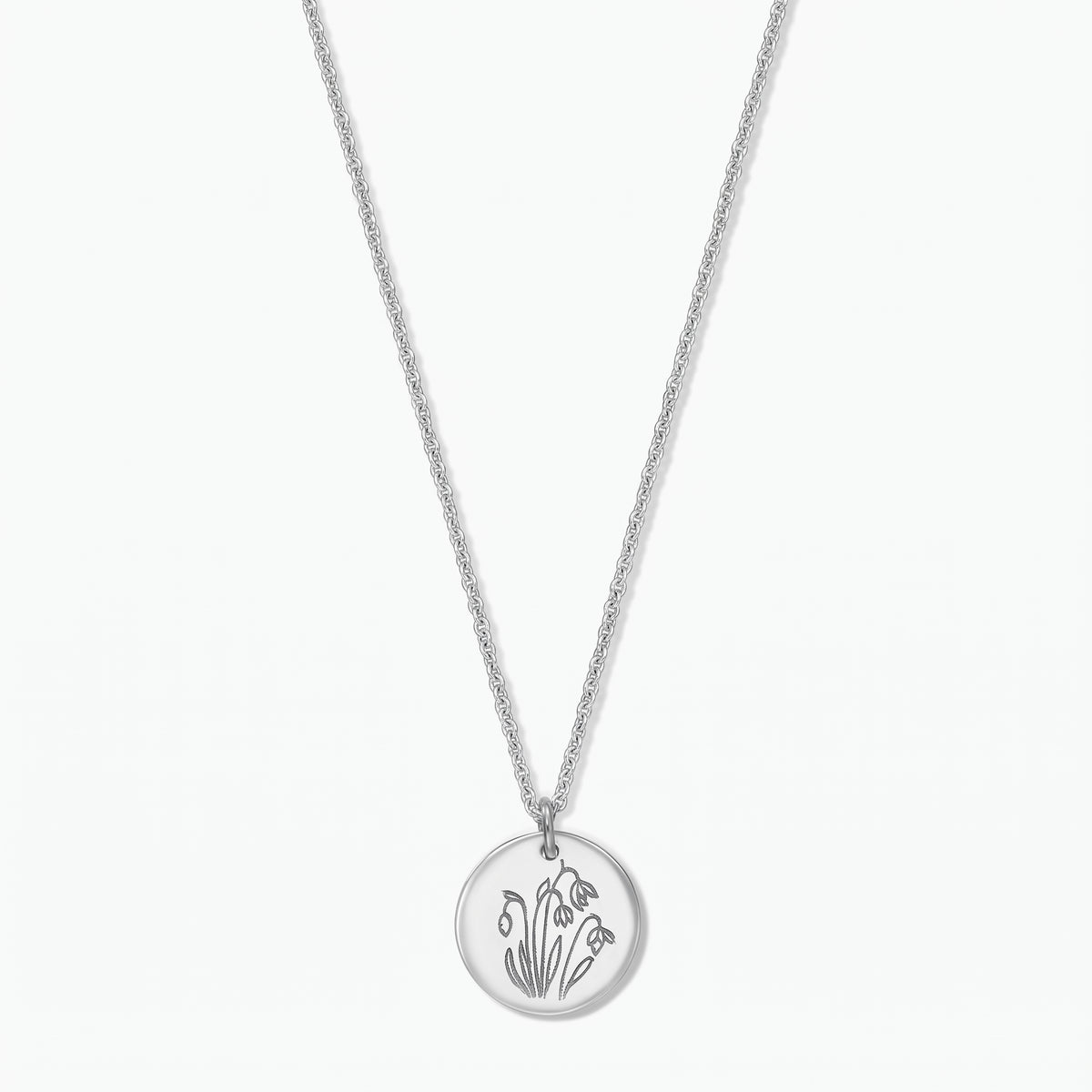 Sterling silver birthflower necklace with a round disc pendant engraved with January snowdrops on a fine chain, isolated on a white background.