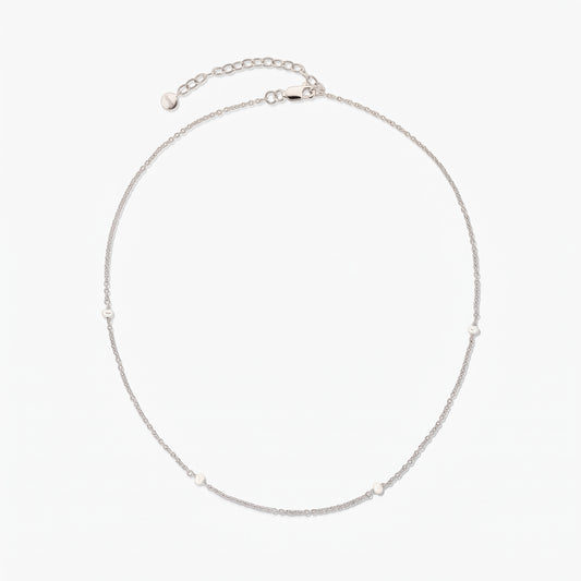 Delicate silver chain necklace with tiny white pearl stations, shown in a circle on a white background with an adjustable extender and lobster clasp.