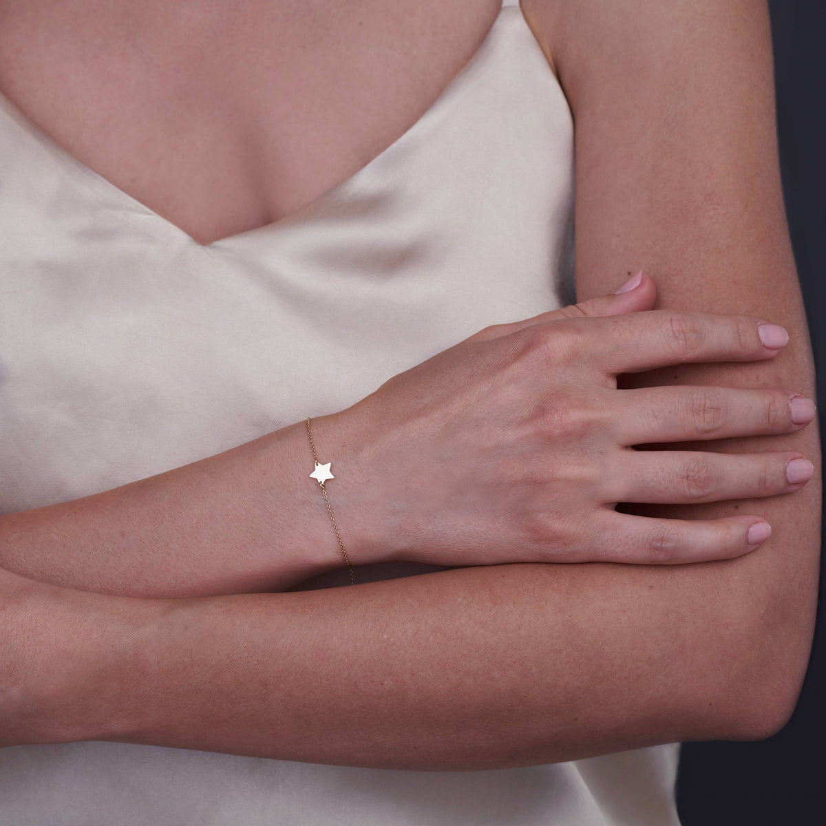 A woman's arm wearing a delicate 14K gold star bracelet against a light-colored satin top.