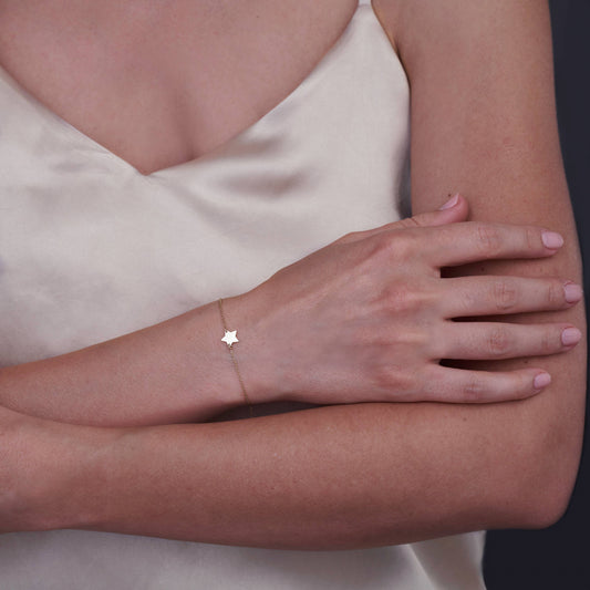 A woman's arm wearing a delicate 14K gold star bracelet against a light-colored satin top.