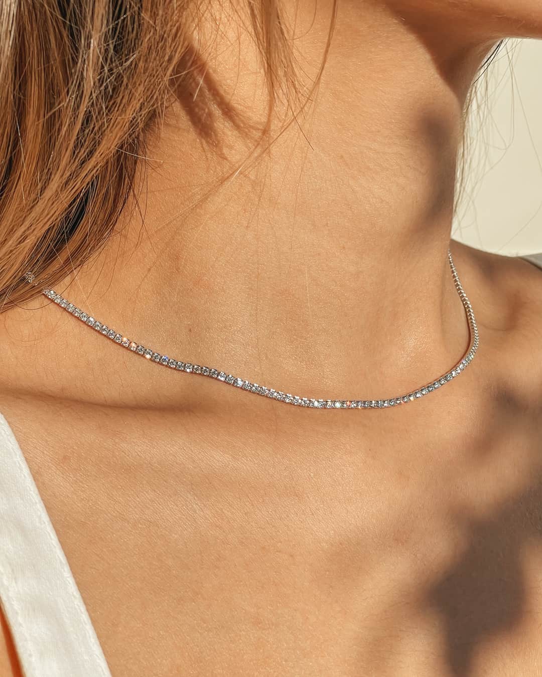 Close-up of a woman's neck wearing a silver tennis necklace with zirconia stones.
